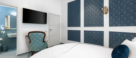 Camera d'hotel con letto bianco, poltrona azzurra e bagno con pareti blu