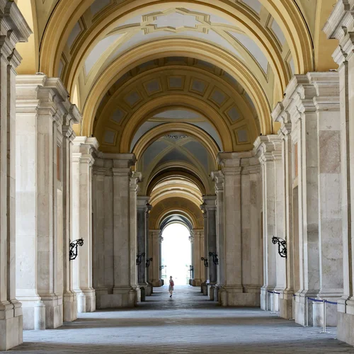 Galleria con archi e colonne in marmo con soffitto decorato e persona sullo sfondo