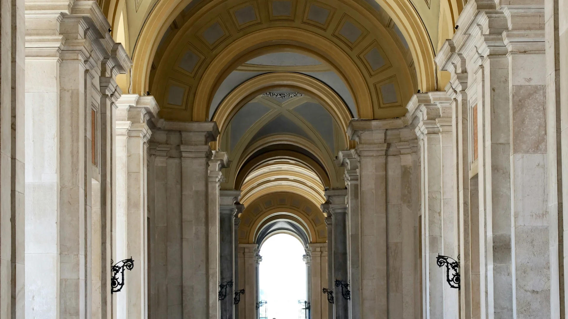 Galleria con archi e colonne in marmo con soffitto decorato e persona sullo sfondo