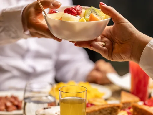 Due persone che si passano una ciotola di frutta fresca a una tavola con pane e succo