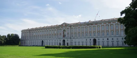 Vista esterna del grande palazzo storico con prato verde e cielo azzurro