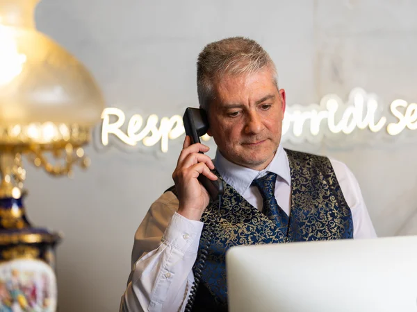 Receptionist in gilet elegante risponde al telefono davanti al computer