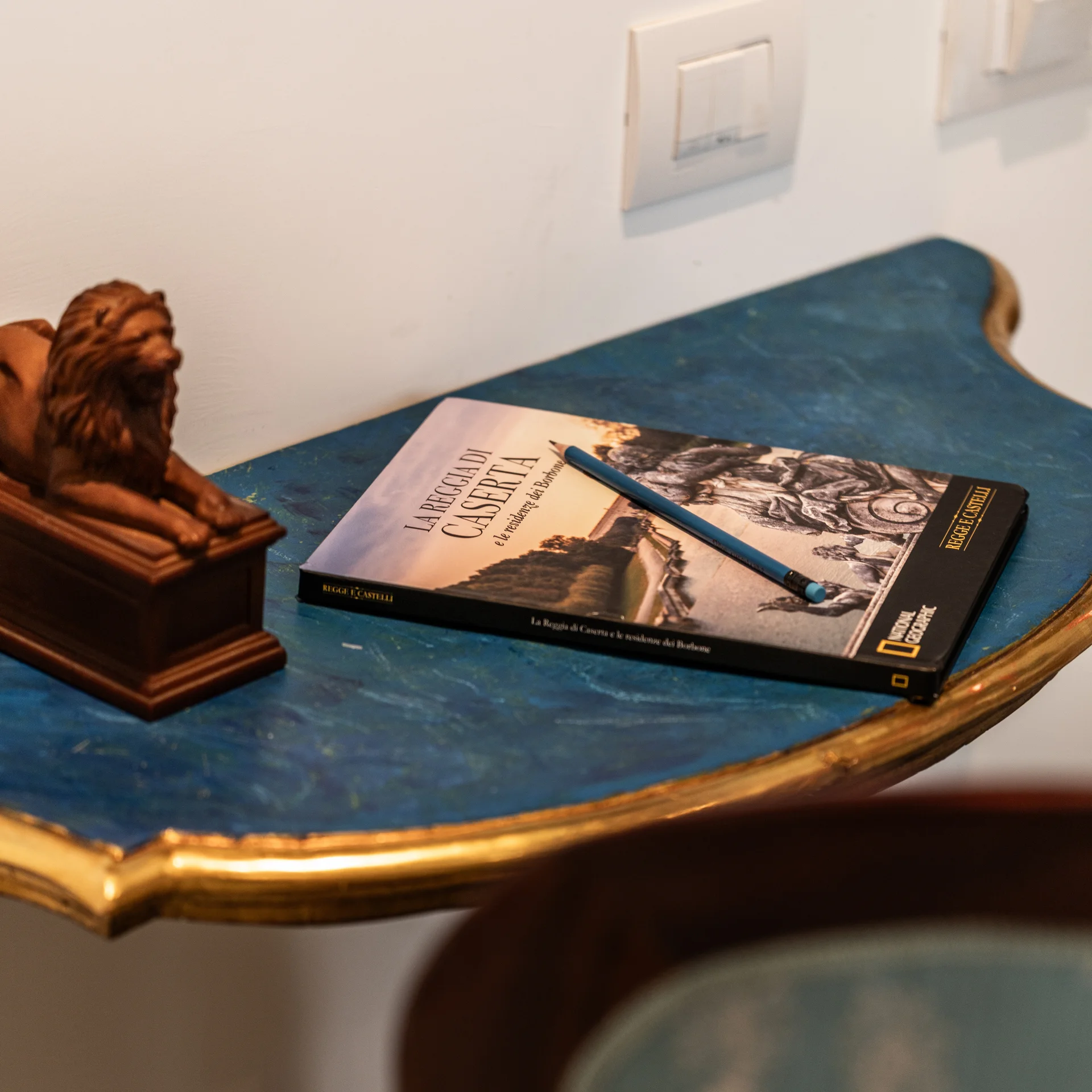 Hotel Regina Caserta · Le domande più frequenti Tavolino blu con libro, matita e statuetta di leone, sedia azzurra decorata