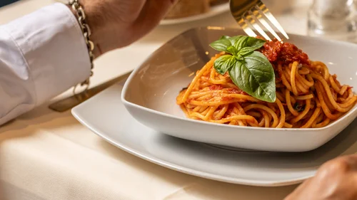Hotel Regina Caserta · Sapori di Campania Persona che mangia spaghetti al pomodoro con foglia di basilico in piatto bianco