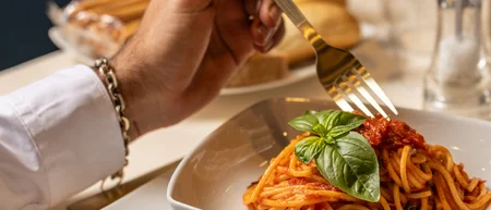 Persona che mangia spaghetti al pomodoro con foglia di basilico in piatto bianco