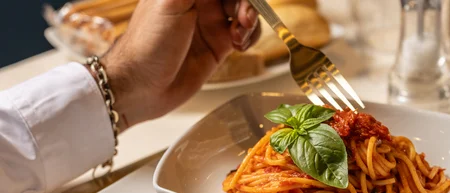 Persona che mangia spaghetti al pomodoro con foglia di basilico in piatto bianco