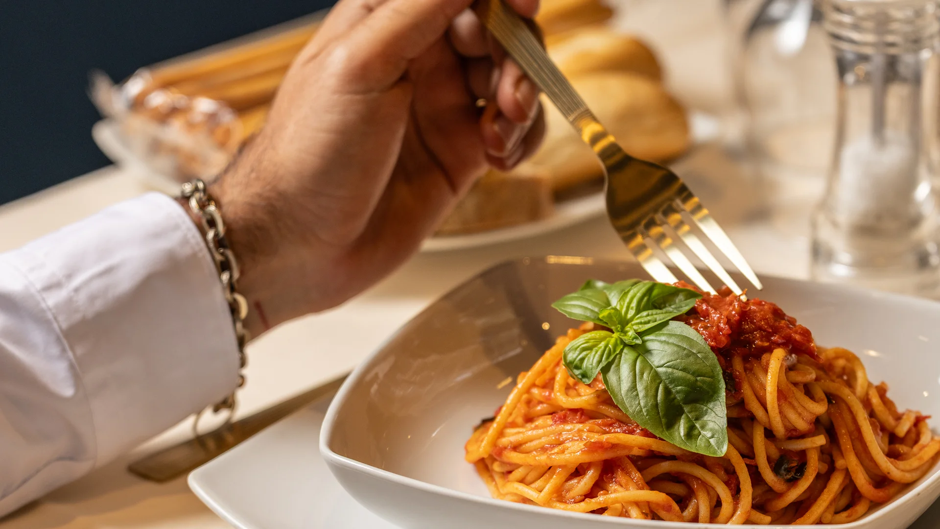 Persona che mangia spaghetti al pomodoro con foglia di basilico in piatto bianco