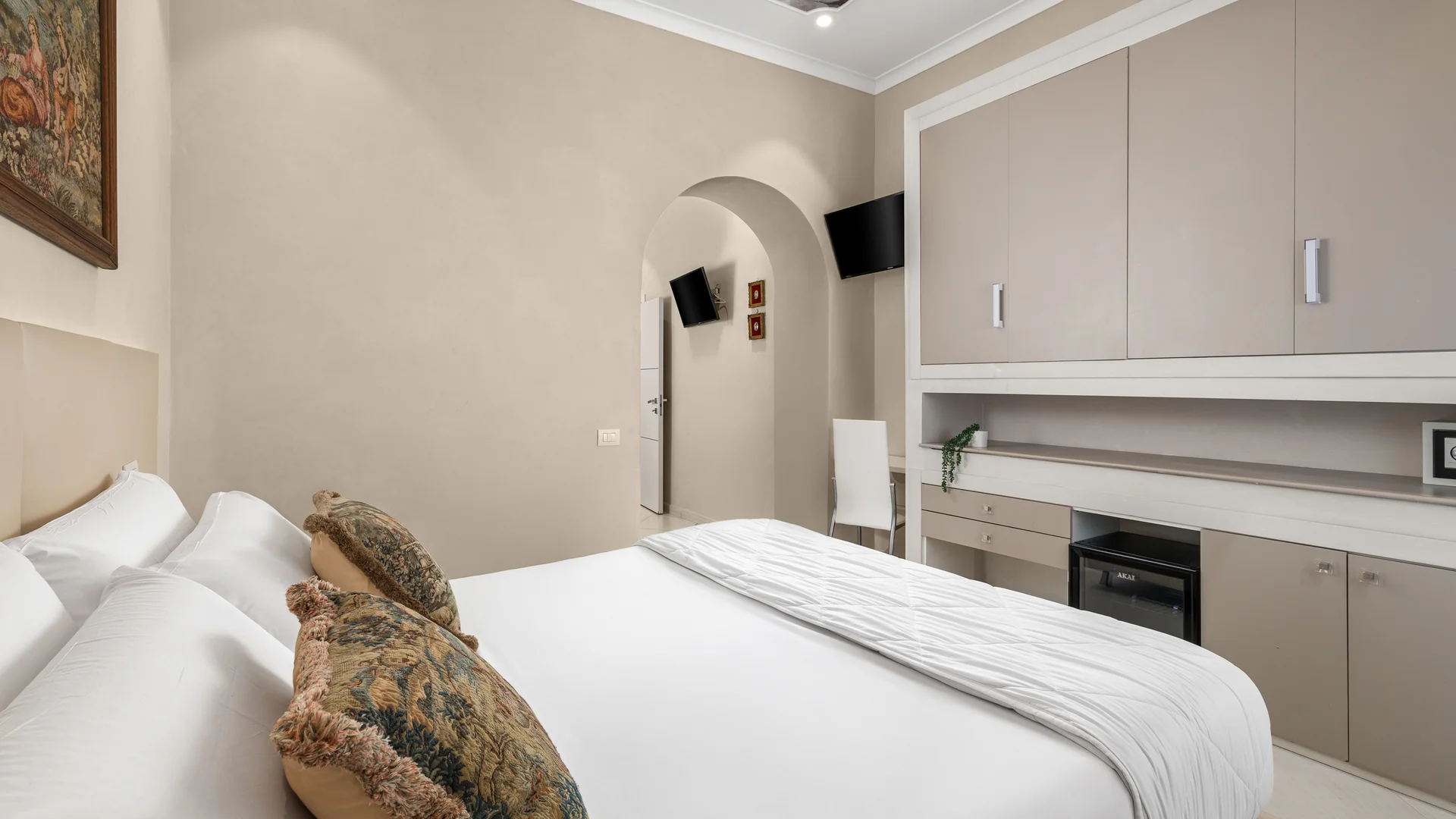 Camera d'hotel moderna con letto matrimoniale, cuscini decorativi, quadro e armadi a muro