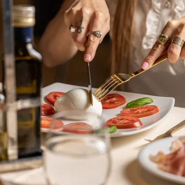 Storie e curiosità su Caserta · Hotel Regina Persona che taglia mozzarella circondata da fette di pomodoro e basilico su piatto bianco
