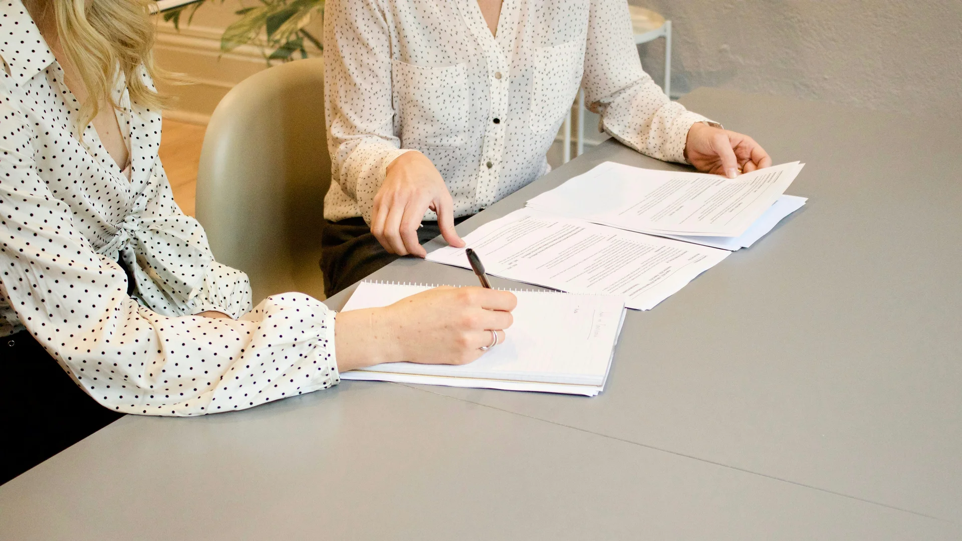 Due donne con camicie a pois che esaminano documenti e prendono appunti a un tavolo