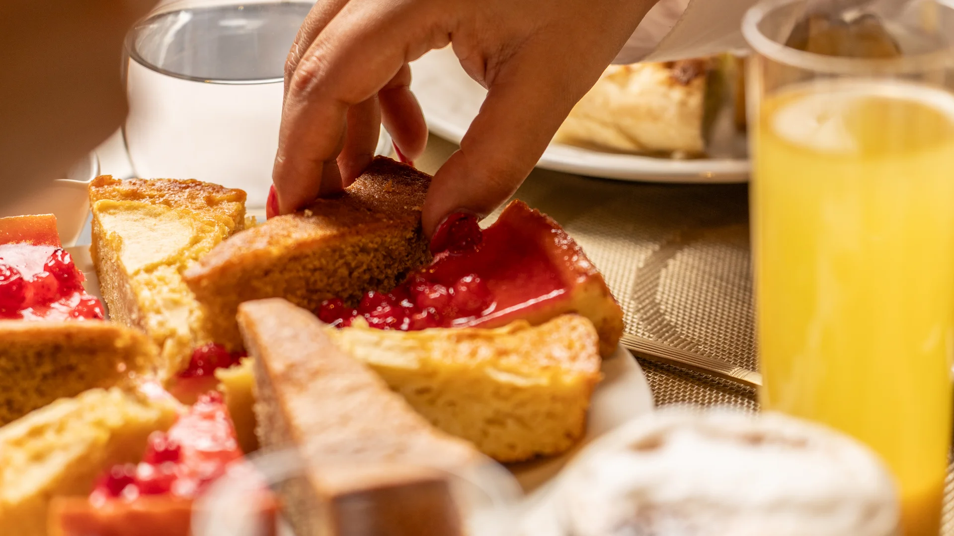 Mano che prende una fetta di torta da un piatto con dolci assortiti a colazione