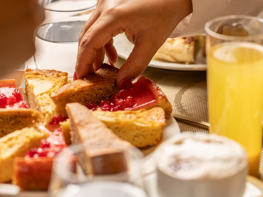 Hotel Regina Caserta · Sapori di Campania Mano che prende una fetta di torta da un piatto con dolci assortiti a colazione