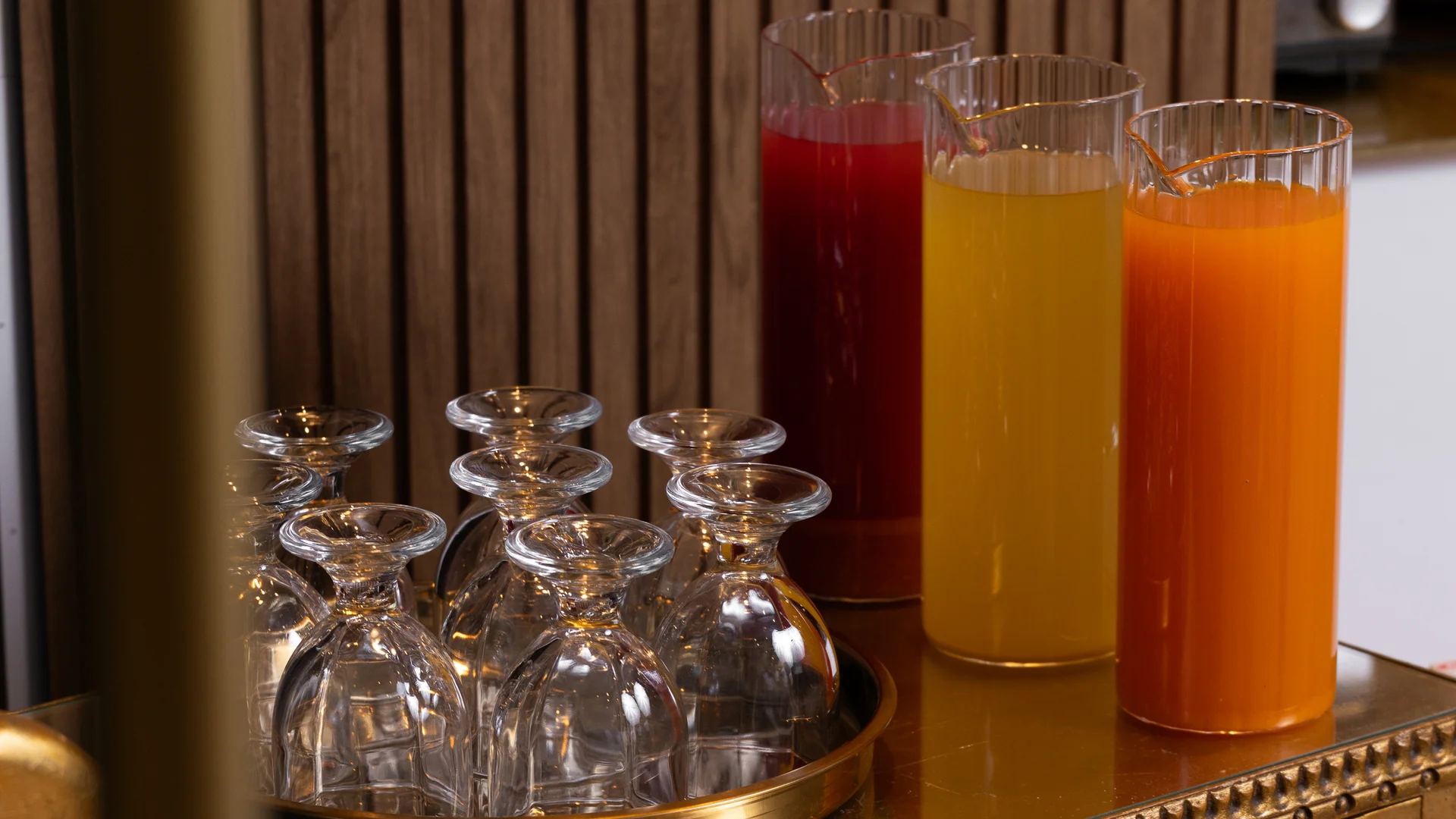 Bicchieri capovolti su un vassoio e tre caraffe di succhi colorati su un mobile dorato