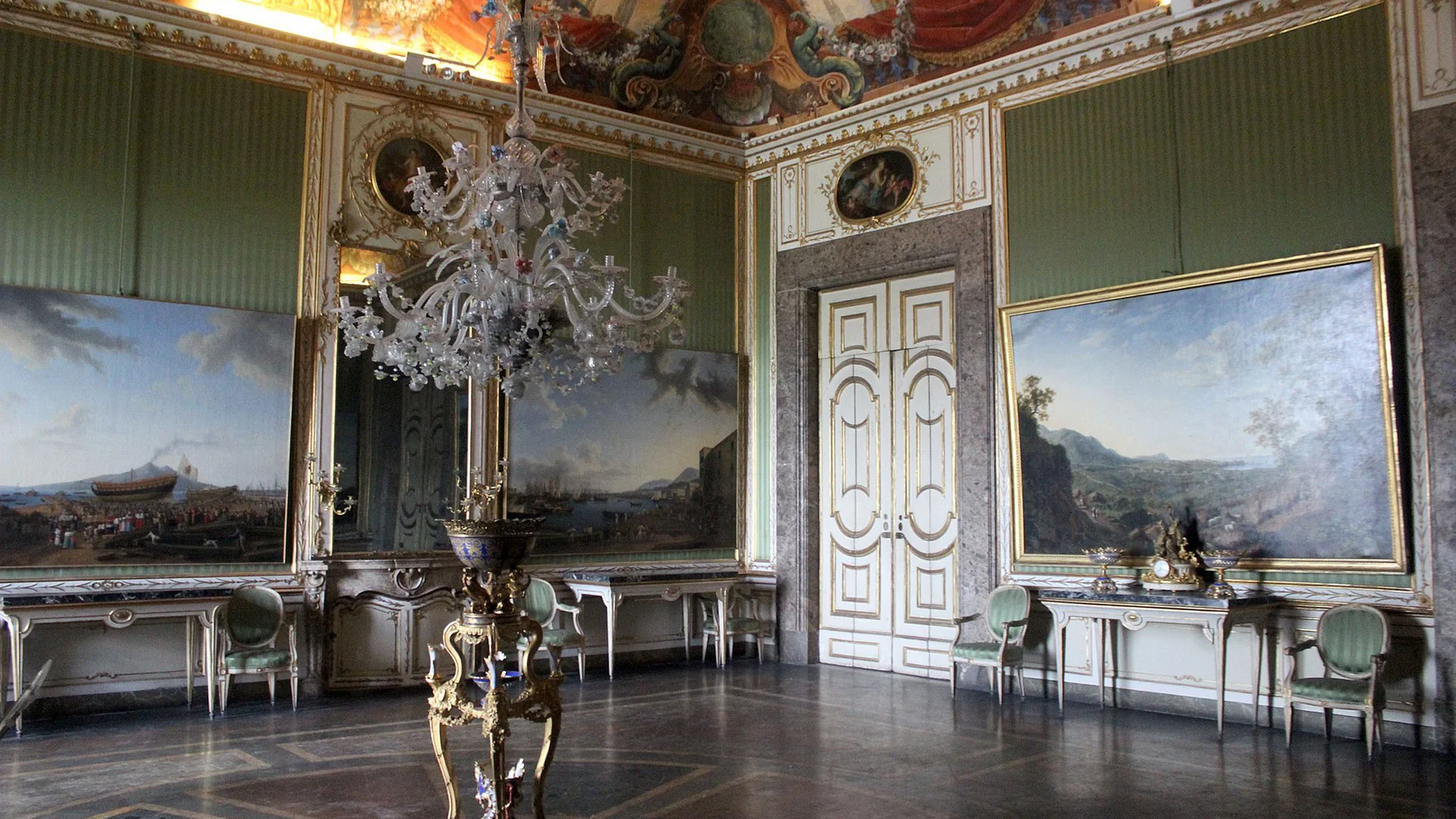 Sala storica con grandi dipinti, lampadario di cristallo e soffitto affrescato