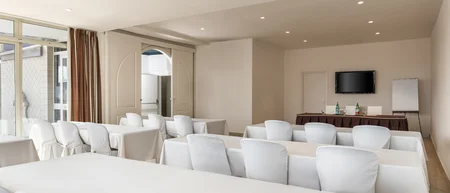 Sala conferenze con sedie bianche e tavoli coperti da tovaglie bianche