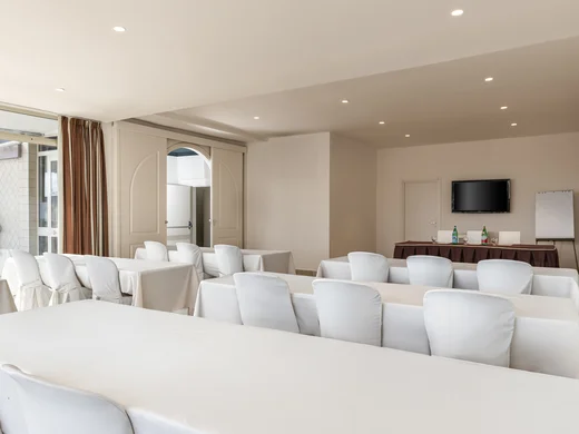 Sala conferenze con sedie bianche e tavoli coperti da tovaglie bianche