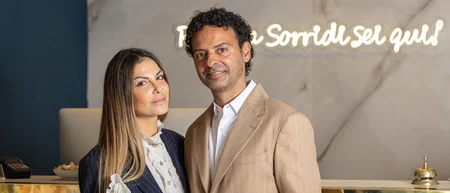 Coppia elegante sorridente alla reception di un hotel con scritta luminosa sullo sfondo
