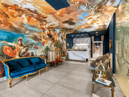 Hotel Regina · Il tuo hotel per coppie a Caserta Hall di hotel con divano blu, affreschi sul soffitto e reception in marmo